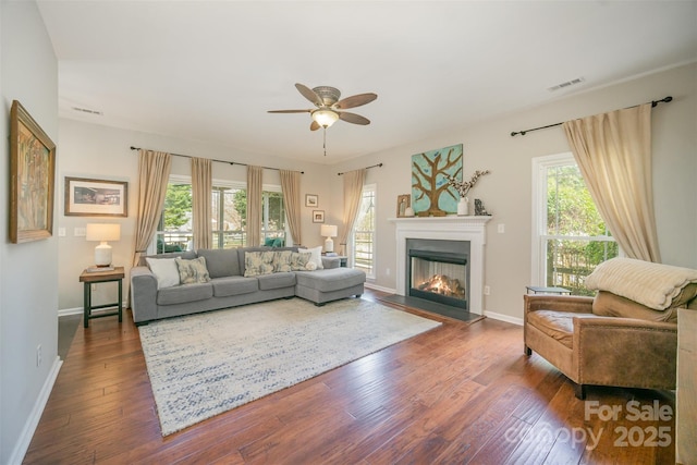 living area with a wealth of natural light, dark wood-style flooring, a glass covered fireplace, and visible vents