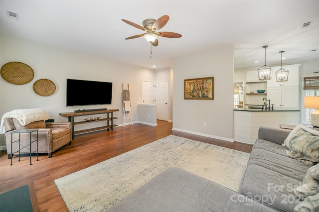 living room with ceiling fan, wood finished floors, visible vents, and baseboards