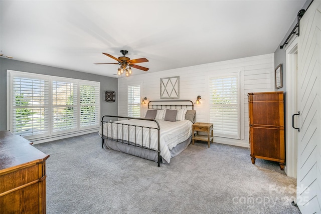 carpeted bedroom with a barn door and ceiling fan