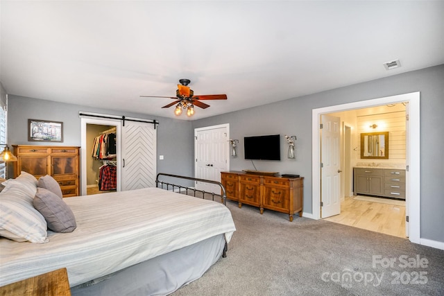 bedroom with a barn door, visible vents, baseboards, and light colored carpet