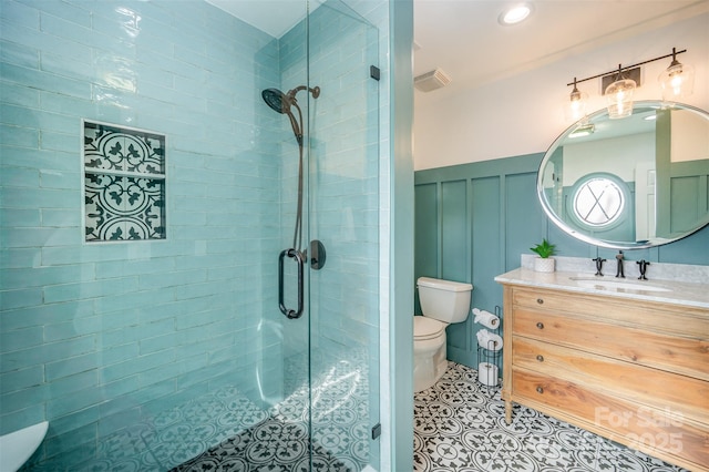 bathroom featuring toilet, a wainscoted wall, vanity, visible vents, and a shower stall