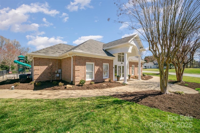 view of home's exterior with a playground, brick siding, fence, roof with shingles, and a lawn