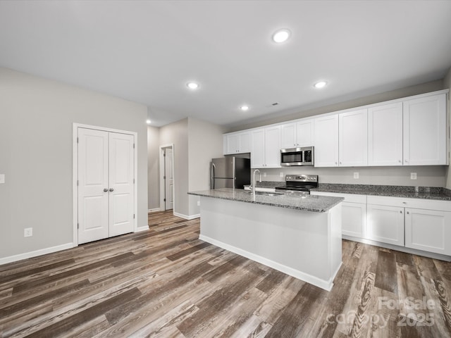 kitchen with sink, appliances with stainless steel finishes, dark stone countertops, white cabinets, and a center island with sink