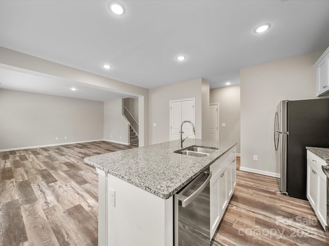 kitchen featuring sink, a kitchen island with sink, white cabinetry, stainless steel appliances, and light stone countertops