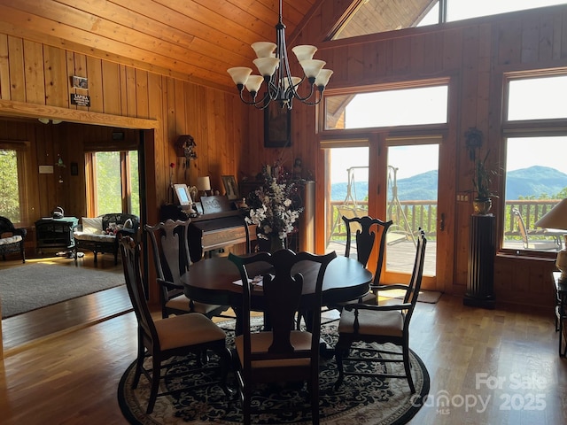 dining space featuring lofted ceiling, hardwood / wood-style floors, a notable chandelier, a mountain view, and wood walls