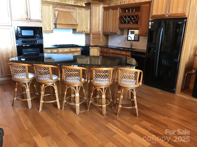 kitchen with a breakfast bar area, sink, wall chimney range hood, and black appliances