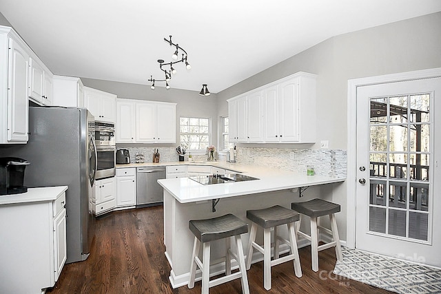 kitchen featuring a breakfast bar, appliances with stainless steel finishes, backsplash, white cabinets, and kitchen peninsula