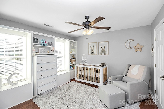 bedroom featuring dark hardwood / wood-style floors, a nursery area, and ceiling fan