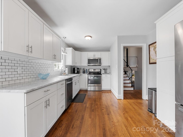 kitchen featuring hanging light fixtures, decorative backsplash, appliances with stainless steel finishes, white cabinetry, and a sink