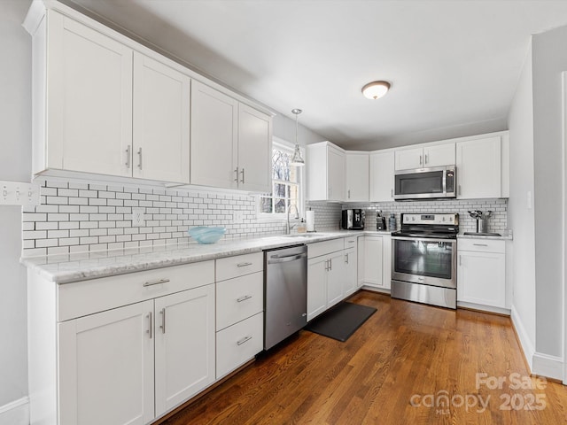 kitchen featuring stainless steel appliances, a sink, white cabinetry, hanging light fixtures, and tasteful backsplash