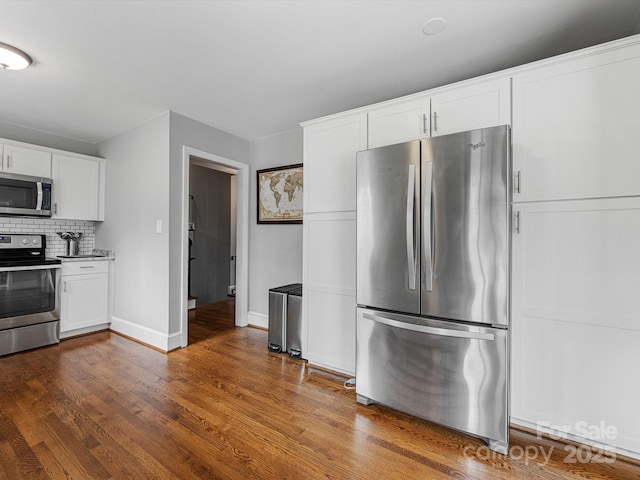 kitchen with dark wood-style flooring, backsplash, appliances with stainless steel finishes, white cabinetry, and baseboards