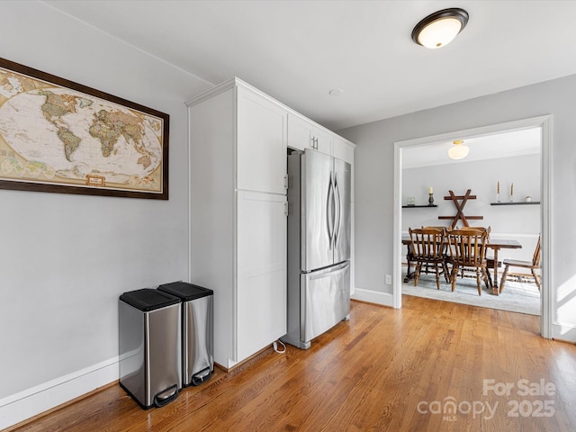 kitchen featuring freestanding refrigerator, baseboards, white cabinetry, and light wood finished floors