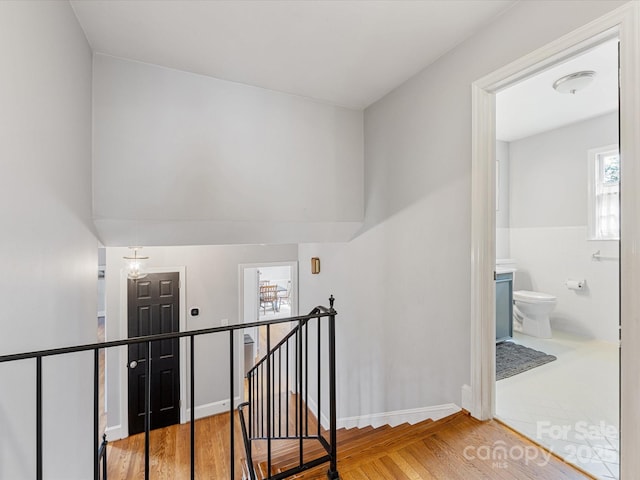 corridor featuring tile walls, wood finished floors, and an upstairs landing