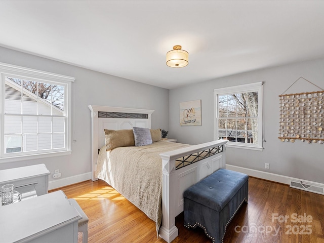 bedroom with multiple windows, visible vents, baseboards, and wood finished floors