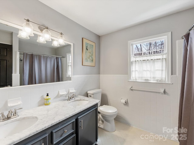 bathroom featuring toilet, double vanity, tile walls, and a sink