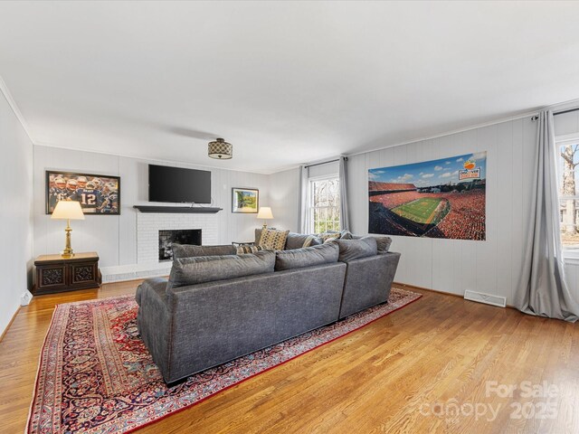 living area with a brick fireplace, crown molding, visible vents, and wood finished floors