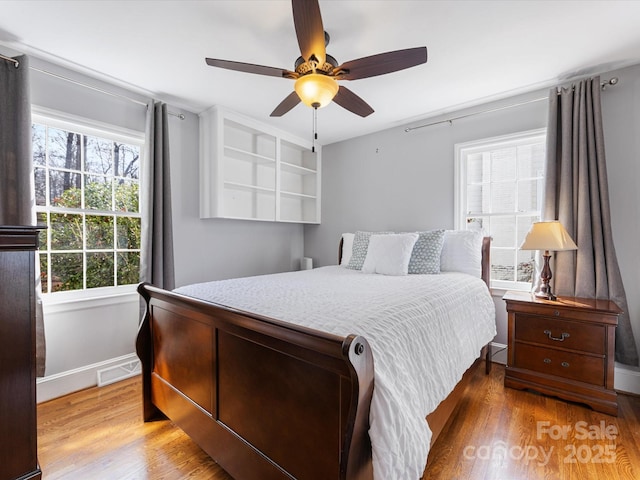 bedroom with a ceiling fan, baseboards, visible vents, and wood finished floors