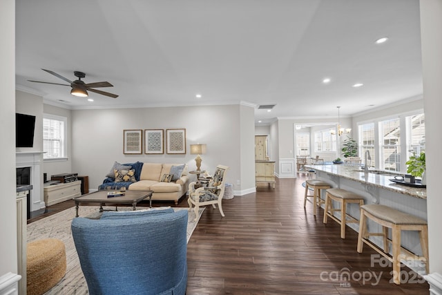 living area featuring recessed lighting, dark wood-type flooring, ornamental molding, a fireplace with flush hearth, and ceiling fan with notable chandelier