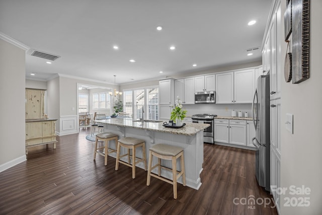 kitchen featuring a kitchen island with sink, stainless steel appliances, visible vents, white cabinetry, and decorative light fixtures