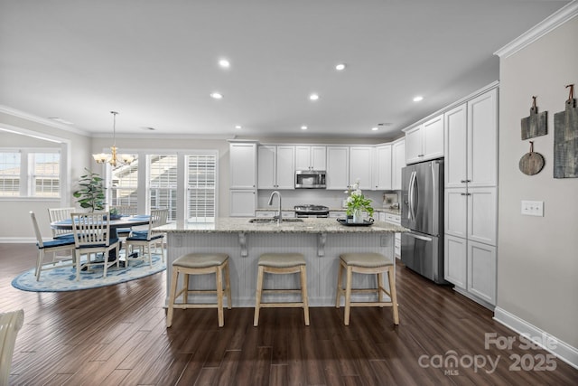 kitchen with stainless steel appliances, light stone countertops, a center island with sink, and pendant lighting