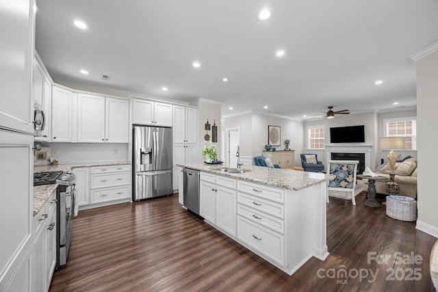 kitchen featuring stainless steel appliances, open floor plan, a kitchen island with sink, white cabinets, and a sink