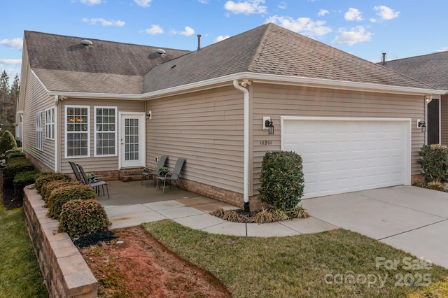 view of property exterior with an attached garage, a shingled roof, concrete driveway, and a patio