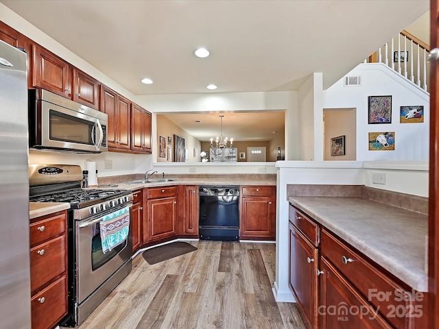 kitchen with pendant lighting, sink, stainless steel appliances, a notable chandelier, and light wood-type flooring