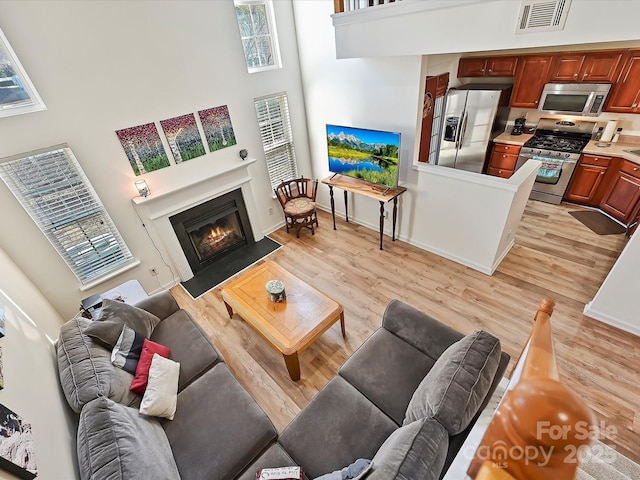 living room with a towering ceiling, a healthy amount of sunlight, and light wood-type flooring