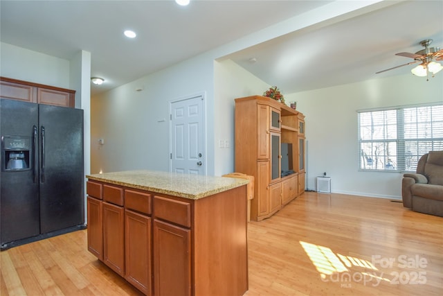 kitchen with black refrigerator with ice dispenser, light hardwood / wood-style floors, a center island, and ceiling fan