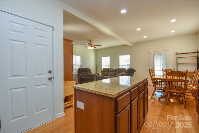 kitchen with ceiling fan, light stone counters, a kitchen island, light hardwood / wood-style floors, and beamed ceiling