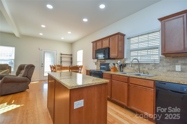 kitchen featuring sink, light stone countertops, a kitchen island, black appliances, and decorative backsplash