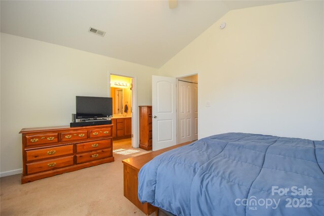 bedroom featuring a closet, lofted ceiling, light carpet, and ensuite bath