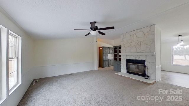 unfurnished living room featuring a stone fireplace, carpet flooring, and a wealth of natural light