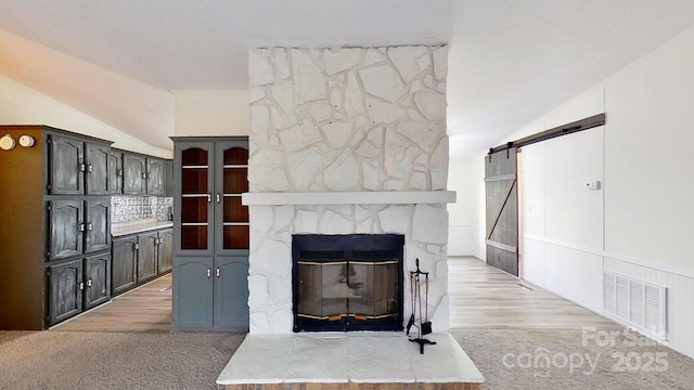 living room featuring a fireplace, vaulted ceiling, light colored carpet, and a barn door