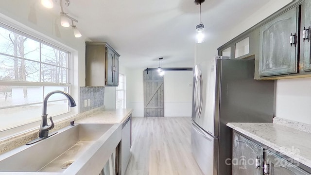 kitchen with sink, backsplash, stainless steel appliances, decorative light fixtures, and a barn door