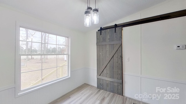 empty room with hardwood / wood-style floors, vaulted ceiling, a barn door, and a wealth of natural light