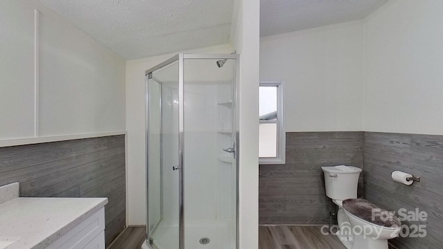 bathroom featuring wood-type flooring, vanity, toilet, a shower with door, and a textured ceiling