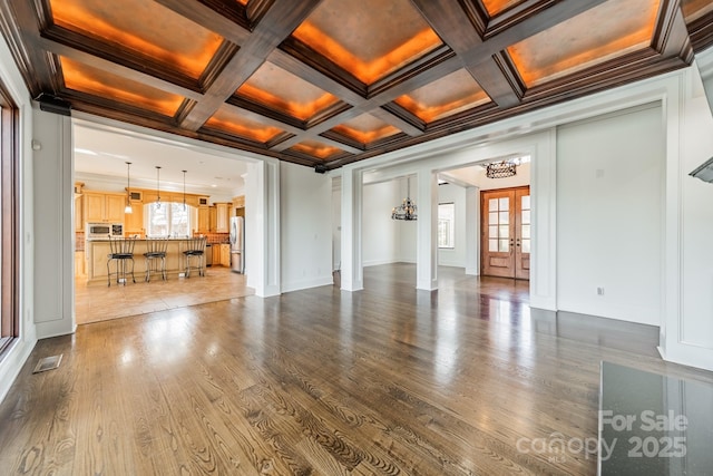 unfurnished living room featuring beam ceiling, coffered ceiling, wood-type flooring, ornamental molding, and french doors