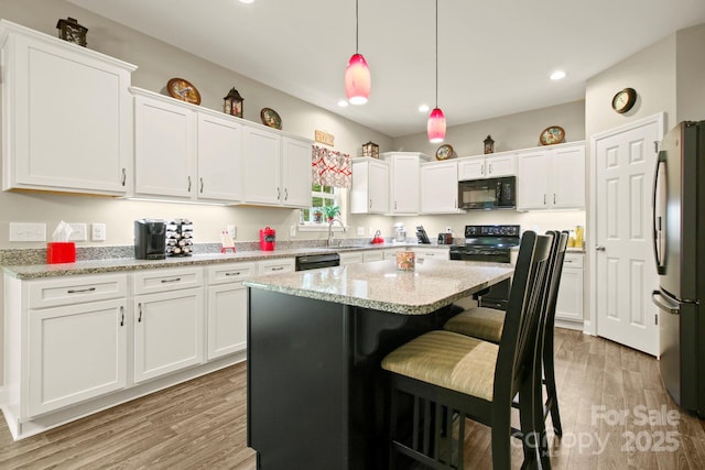 kitchen with light hardwood / wood-style flooring, white cabinetry, a center island, black appliances, and decorative light fixtures