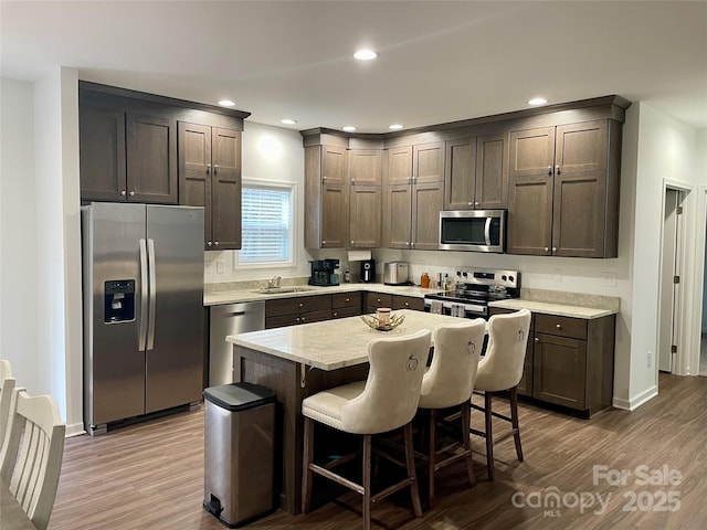 kitchen with dark brown cabinetry, a kitchen bar, sink, appliances with stainless steel finishes, and a kitchen island