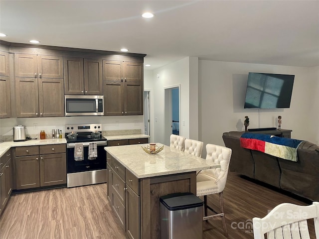 kitchen with a kitchen bar, a center island, dark brown cabinets, appliances with stainless steel finishes, and light hardwood / wood-style floors