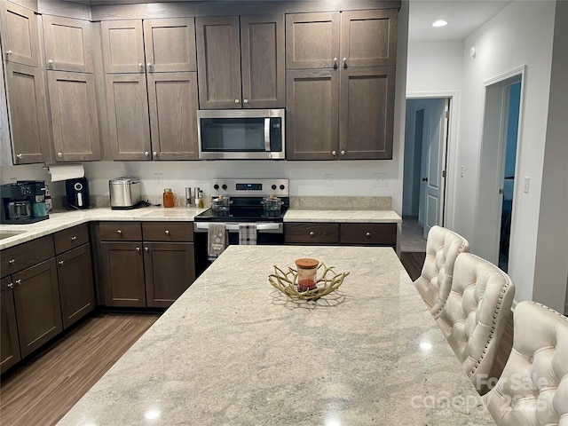 kitchen with light stone counters, dark hardwood / wood-style flooring, dark brown cabinetry, and appliances with stainless steel finishes