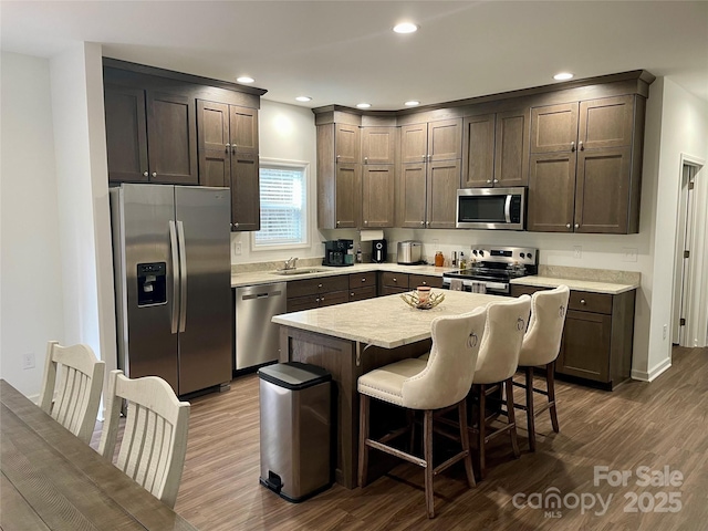 kitchen featuring dark brown cabinetry, a kitchen breakfast bar, dark hardwood / wood-style flooring, a kitchen island, and stainless steel appliances