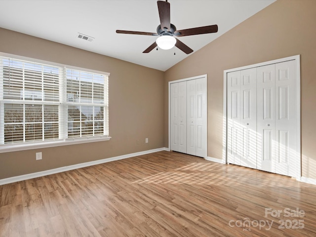 unfurnished bedroom featuring vaulted ceiling, ceiling fan, light hardwood / wood-style floors, and two closets