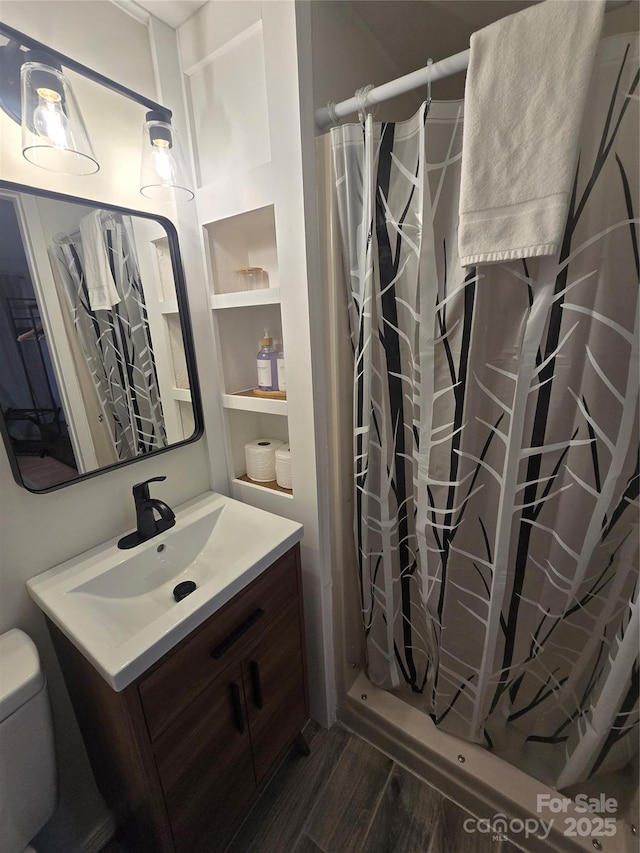 bathroom with hardwood / wood-style flooring, walk in shower, vanity, and toilet