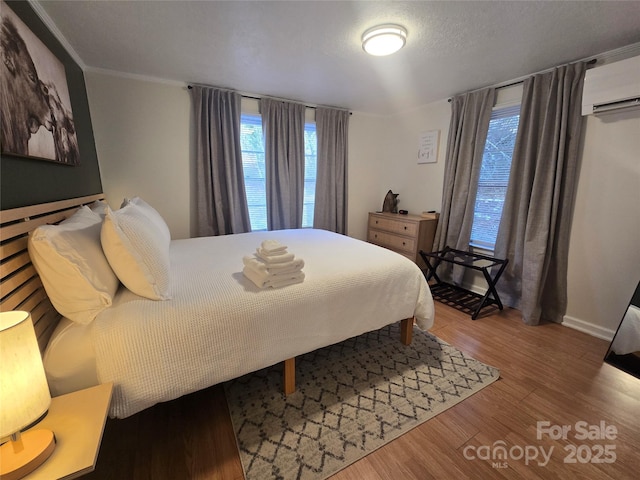 bedroom featuring crown molding, hardwood / wood-style flooring, a wall unit AC, and a textured ceiling