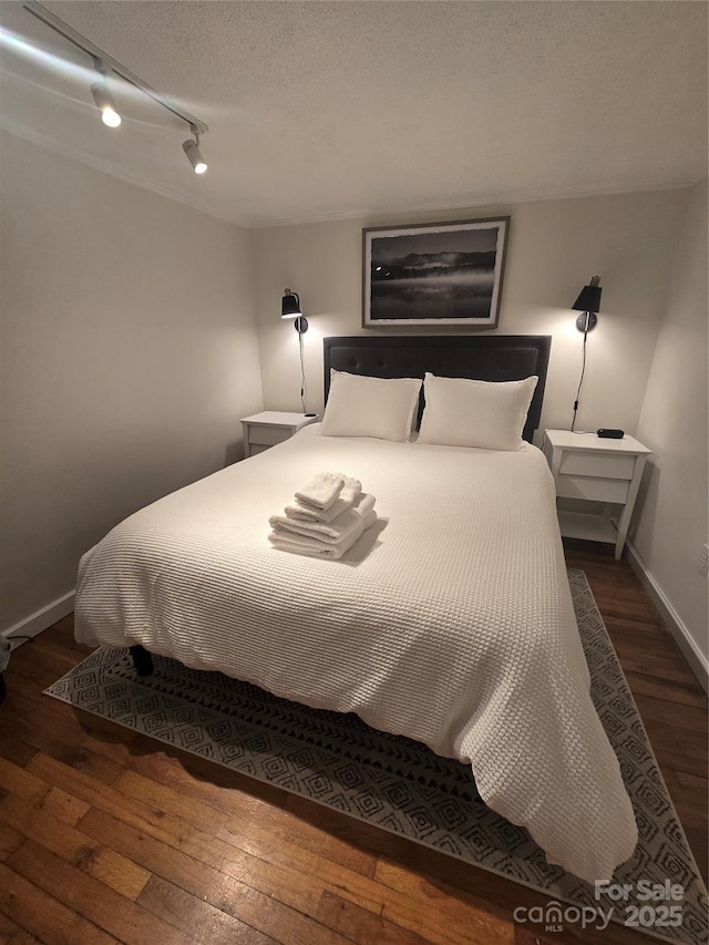 bedroom with rail lighting, a textured ceiling, and dark hardwood / wood-style flooring