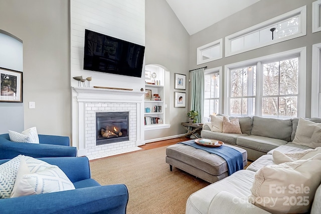 living room featuring wood-type flooring, a brick fireplace, high vaulted ceiling, and built in shelves