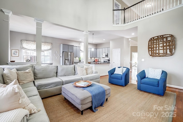 living room with a towering ceiling, decorative columns, and light wood-type flooring