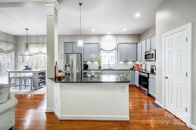 kitchen with decorative light fixtures, a center island, light wood-type flooring, stainless steel appliances, and decorative backsplash